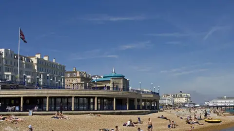 A pebbled beach with many visitors sunbathing. 