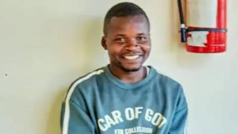 The Citizen A head and shoulder image of Shedrack Chaula smiling at the camera. he is wearing a green sweatshirt and part of a fire extinguisher can be seen on the wall behind him.