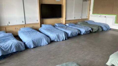 A row of blow-up beds with blue duvet and pillow covers on a grey floor.