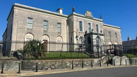 Downpatrick Crown Court. It is a grey Georgian style building with large windows.