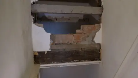 Marion Heard An area above a staircase where building work has been left incomplete, exposing bare brick and rough edges. 