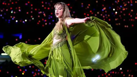 Getty Images Taylor Swift in a flowing green dress during her Eras Tour on stage