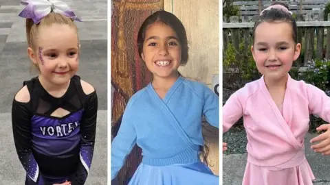 Family handouts Three children standing side by side, each wearing different outfits. Elsie is in a black and purple cheerleading uniform, Alice wears a light blue wrap cardigan and matching skirt, while Bebe wears a pink wrap cardigan with a matching skirt.