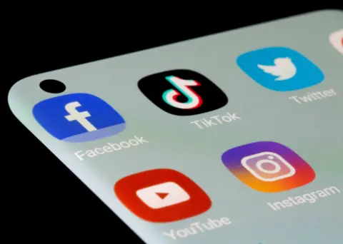 A close up of a mobile phone showing social media app logos. Top row: Facebook, TikTok, Twitter. Second row: YouTube, Instagram.