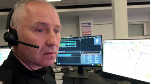 A man sits in front of a computer with a headset on