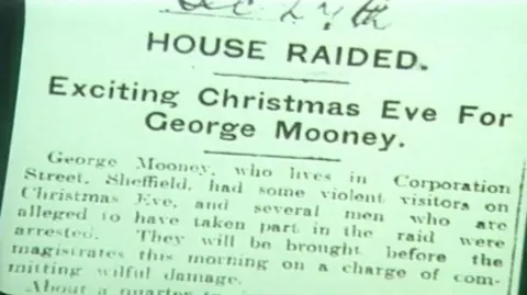 Supplied The image shows a close-up of an old newspaper clipping reproduced in black and white with a slight greenish tint. At the top of the clipping, a bold headline reads “HOUSE RAIDED”. Beneath it, a larger subheading states “Exciting Christmas Eve For George Mooney”. Below the headline is a block of smaller printed text laid out in narrow newspaper columns. The text refers to George Mooney, gives a street location in Sheffield, and describes a raid carried out on Christmas Eve, mentioning visitors, alleged involvement and court proceedings.