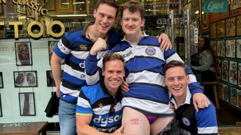 Image of Ben Craven and friends, showing off his COYB 2024 Champions tattoo on his thigh