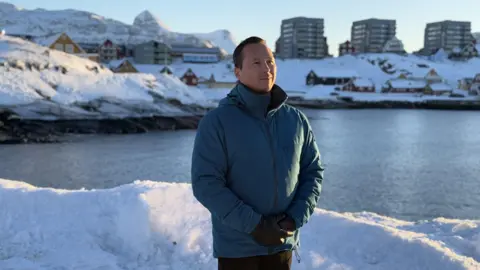 Kuno Fencker standing by the water in a green jacket with the sun shining on the side of his face