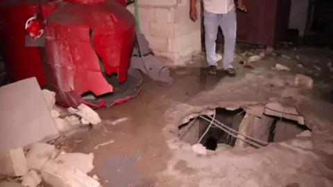 Al-Ikhbariya al-Suriyah TV Syrian regional TV Al-Ikhbariya al-Suriyah shows a Syrian man standing next to a hole in the roof of a building that was reportedly hit in an Israeli strike in the Syrian port of Tartous on September 9. 2024)