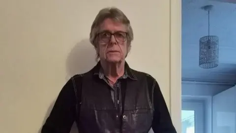 Kelvin Pratt Kelvin Pratt is wearing a black leather jacket and looking at the camera. He has dark-framed glasses and is inside a house.