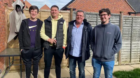 LAURENCE DENIS Four men stood next to each other in a garden