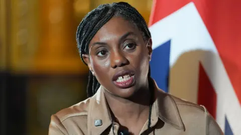 PA Media Kemi Badenoch looks to the camera while speaking during a press conference with the Union flag in the background, in London on 5 February.