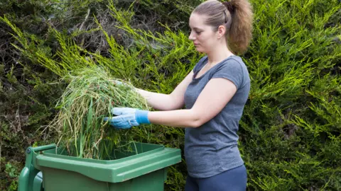 Getty Images woman using green wheelie bin