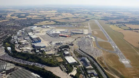 LONDON LUTON AIRPORT An aerial view of an airport and its surrounding area, likely taken from an aircraft or helicopter. The airport has one runway. 