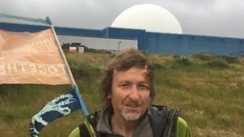 Contributed Chris Wilson standing in front of the Sizewell B building, a large blue building with a white dome on top.