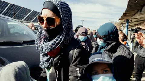 Getty Images People walk beside a van with their belongings for departure at the Roj camp in al Malikiyah, Syria on 15 February 2026