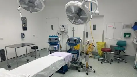 BBC/ Mark Denten A new stark white operating theatre with a bed and machines.