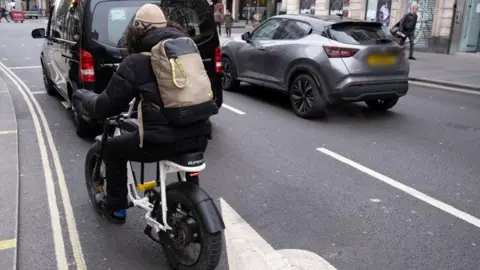 A delivery driver riding an e-bike on a street in London 