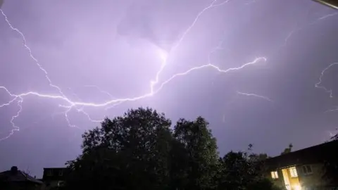 Tim/Weather Watchers Fork lightning fills a purple sky with the silhouette of trees below