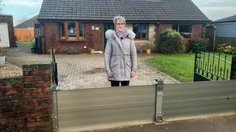 Elaine Merrick-Reed stands behind the flood barrier across her driveway