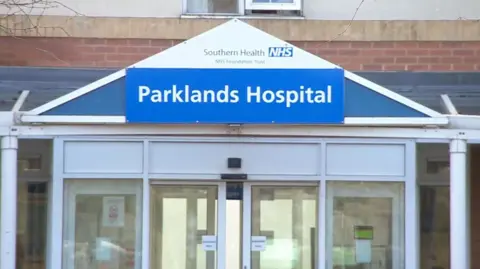 The entrance to Parklands Hospital. The name of the hospital is on a sign above white sliding doors.