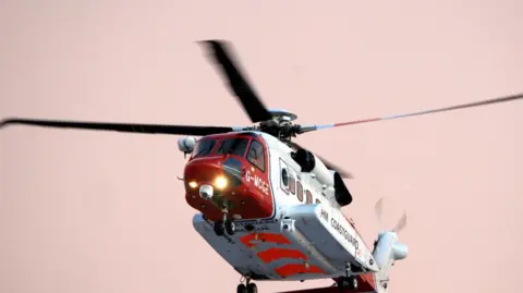 Darrin Stevens Close-up shot of a red and white coastguard helicopter searching the area.