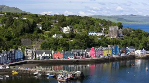 Getty Images The waterfront at Tobermory on the Isle of Mull. Various fishing boats are in the water, while a row of brightly coloured homes are visible on the front.