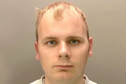 Lincolnshire Police A police custody shot showing the head and shoulders of a man with short blonde hair and blue eyes, with a neutral expression on his face. He is wearing a light-grey T-shirt and the photo is taking against a grey background.
