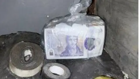 Police handout A plastic bag containing a stack of £20 notes alongside some tape.