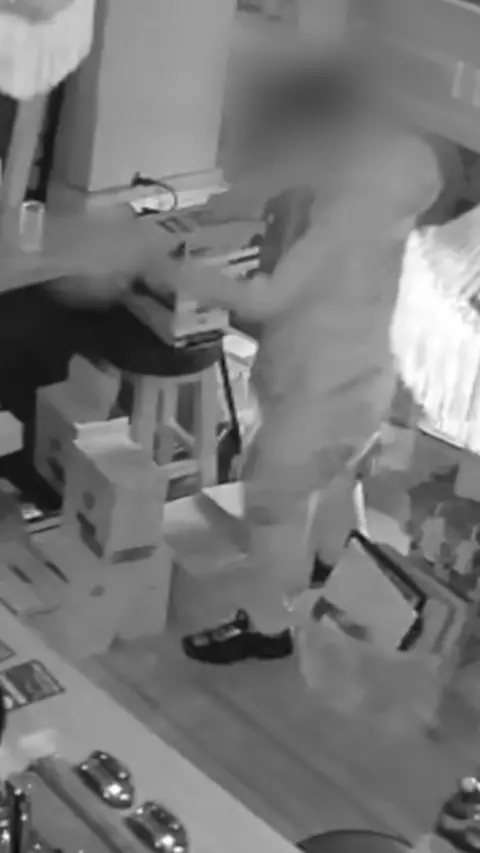 A black and white CCTV image showing a man inside a pub. His face and hands are blurred.