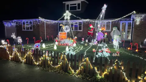 Adrian Harms/BBC A house in Milden Gardens, Frimley Green, covered extensively with Christmas decorations. There are several sets of lights, candy canes, and inflatable snowmen, Santa Claus, and reindeer.