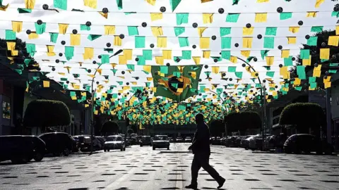 Getty Images A man crosses a wide avenue decorated with green and yellow bunting in Brasilia, Brazil