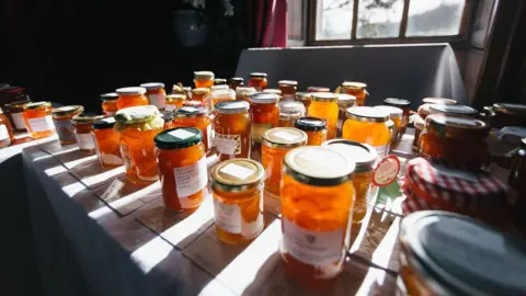 Various-sized jars of orange marmalade on top of a table.