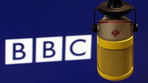 A white BBC logo on a dark blue background, with a yellow vintage-style microphone in the foreground