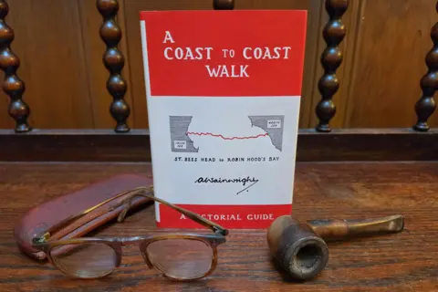 Chris Butterfield A red book entitled "A Coast to Coast walk - a pictorial guide" with a map of the trail on the front cover, behind brown glasses and a brown pipe