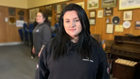 BBC Emma Lewis, black long hair wearing a black hoodie with a Counter Force logo.