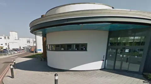 The glass-fronted entrance to Antelope House is sheltered by a projecting roof and has a curved white wall in the middle of it. In the background is Royal South Hants Hospital.