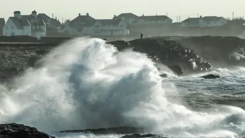 Huge wave crashes on to shore watched by spectators