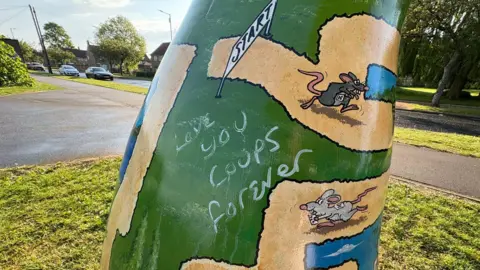 Graffiti daubed on a green-coloured rat sculpture, which shows a number of rats  making their way through a maze.