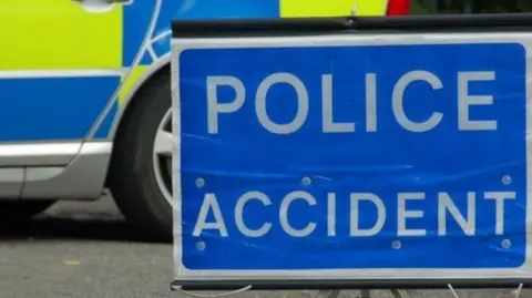 A sign reading "police accident". There is a police car behind it