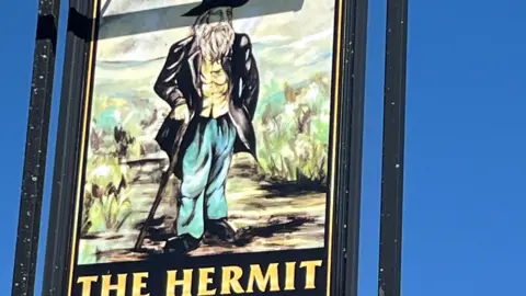 A pub sign showing what is obviously meant to represent an eccentric old man with flowing beard, walking cane and colourful though scruffy attire