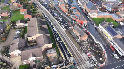 An aerial shot of Bedlington station with houses on either side and the railway line running through the centre. Some construction fencing is in place on one side of the station