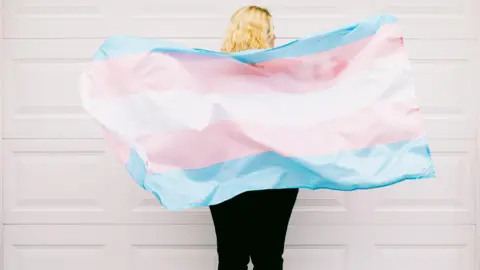 Getty Images A person holding a transgender flag that is blue white and pink.