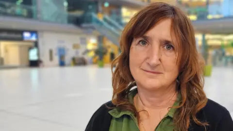 Lucy Galvin is sitting in The Forum in Norwich looking at the camera. She has a black light cardigan over a green shirt.