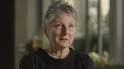 Rosemary Agnew, a woman with short grey hear, wearing a black top and pearl earrings and necklace.