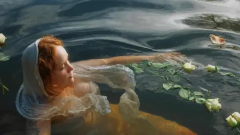 Meg is floating in the Avon with roses on the water.