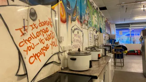 Pots and other cooking utensils in front of a wall with colourful artwork