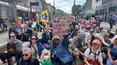 Leith demo - hundreds of protesters are sitting in a road with anti-racism banners