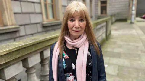 Woman wearing a pink scarf smiles at camera