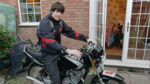 Richard Cheshire A man in leathers on a bike with an L plate on it. He has dark brown hair.
